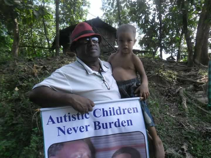 Foundation leader holding a child with an 'Autistic Children Never Burden' sign